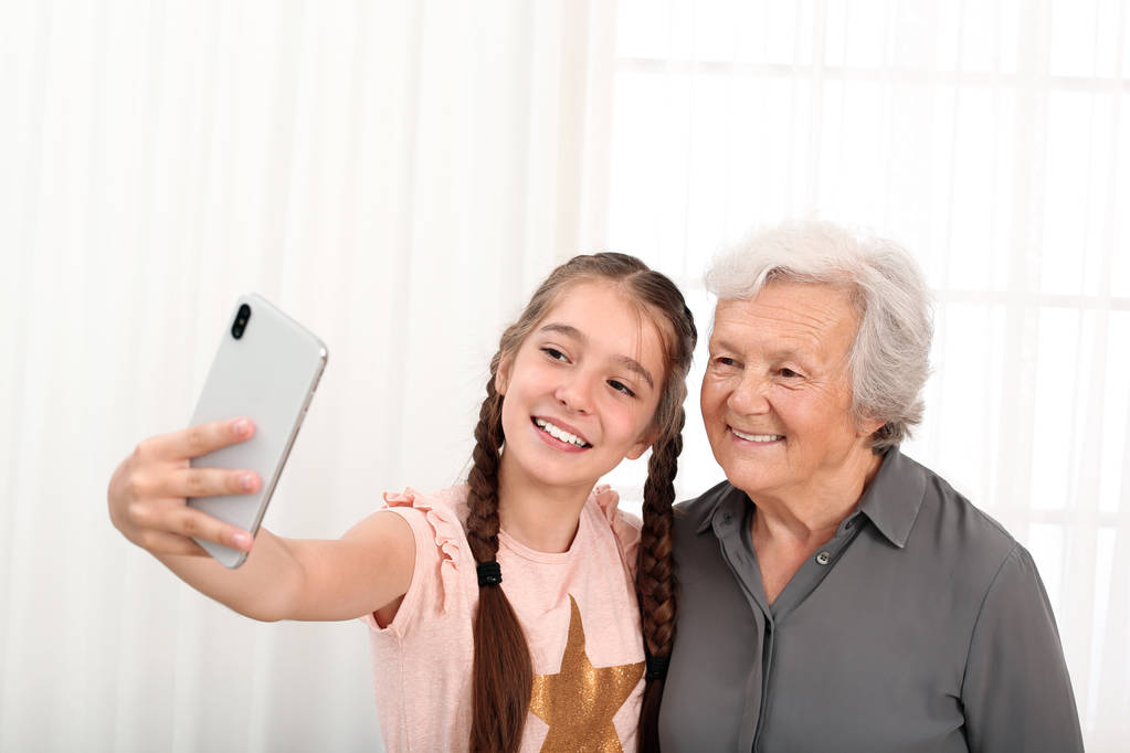Ευτυχισμένο χαριτωμένο κορίτσι λήψη selfie με τη γιαγιά της στο σπίτι - Φωτογραφία, εικόνα