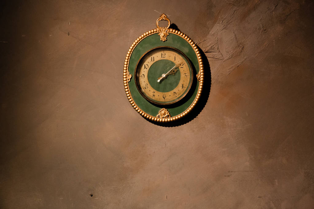 Gold vintage clock with arabic numbers. Beautiful green frame clock hanging on the brown wall. Antique round wall timepiece. Copyspace - Photo, Image