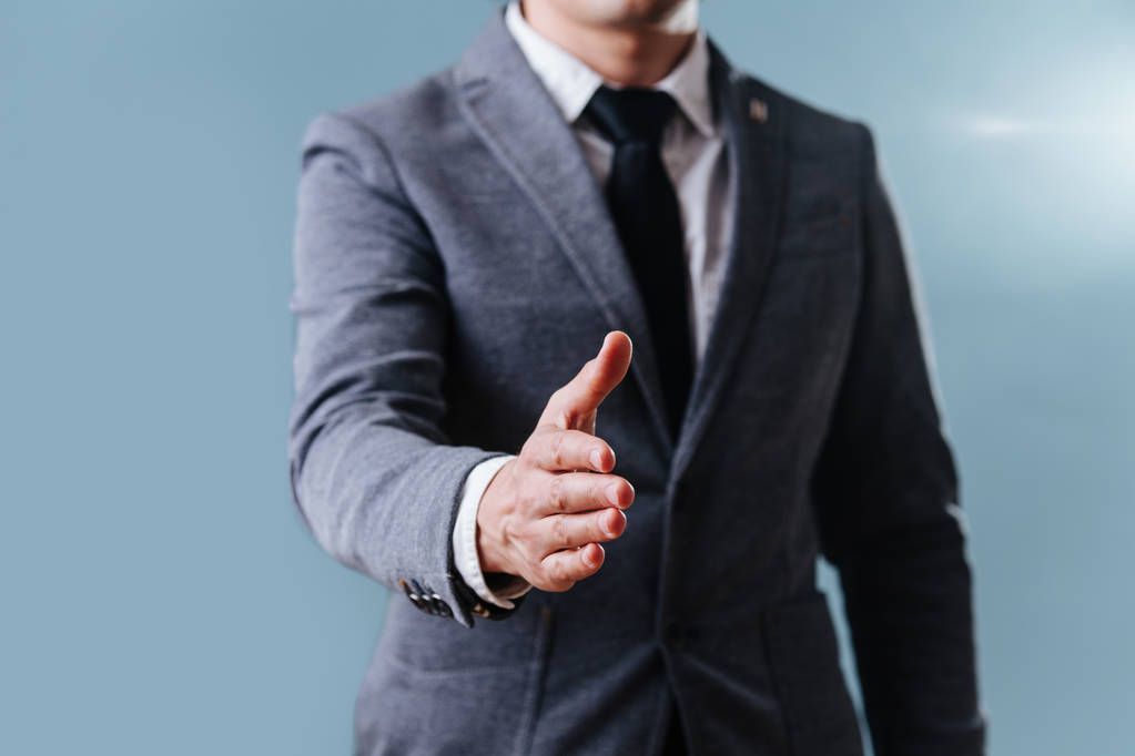 Бізнесмен у костюмі, розтягнута рука, готовий для рукостискання на синьому фоні
 - Фото, зображення