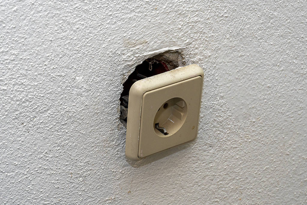 Een vuile witte socket viel uit de muur en hangt op draden. Reparatie in het huis van oude euro Sockets. - Foto, afbeelding