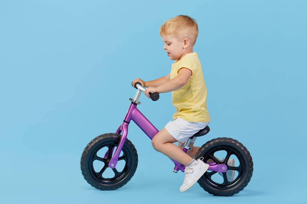 Malý chlapec se učí udržet rovnováhu při jízdě na kole. Stylové dítě ve žlutém tričku na modrém pozadí - Fotografie, Obrázek