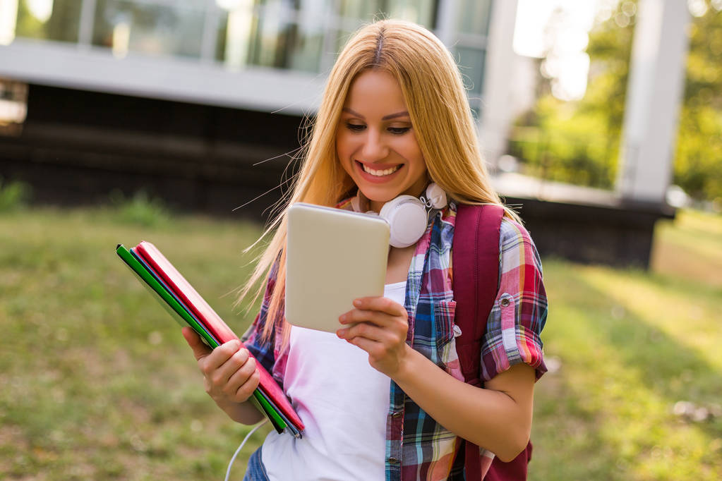 Female student with headphones using digital tablet outdoor. - Photo, Image
