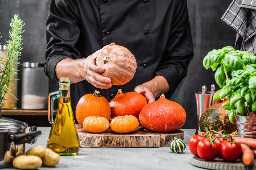oříznutý záběr kuchaře drží zralé dýně v kuchyni  - Fotografie, Obrázek