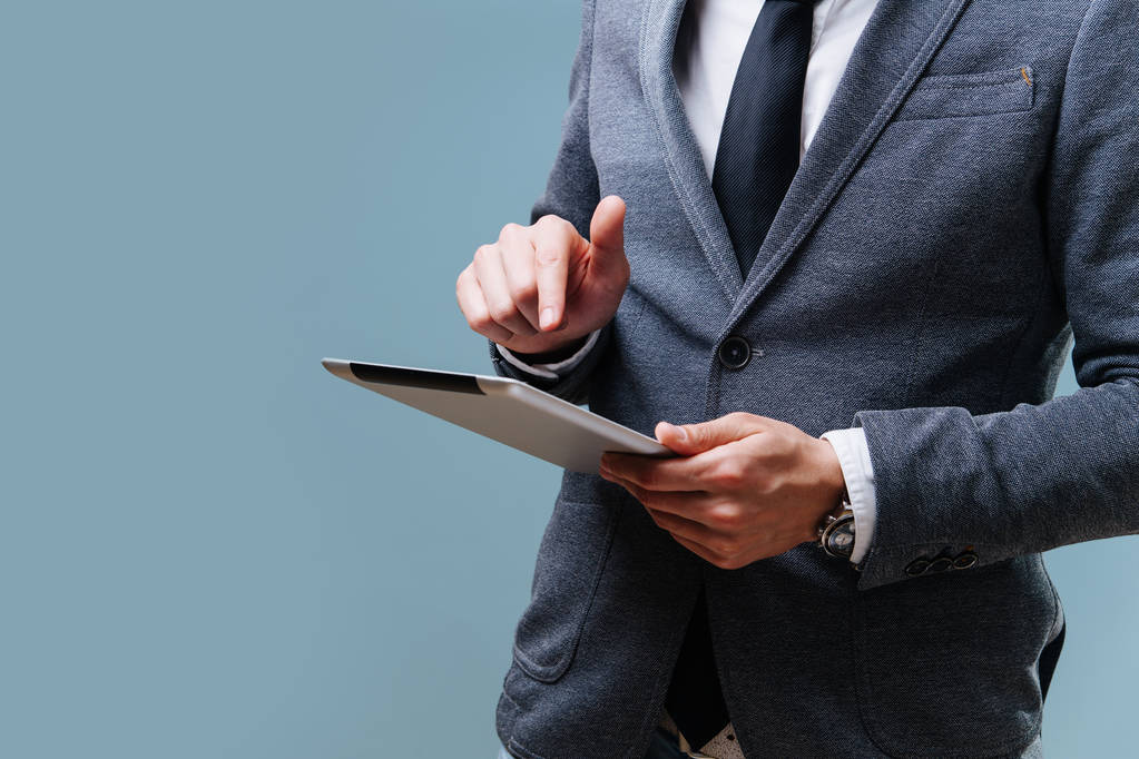 Geschäftsmann wählt auf seinem Tablet vor blauem Hintergrund eine App aus - Foto, Bild