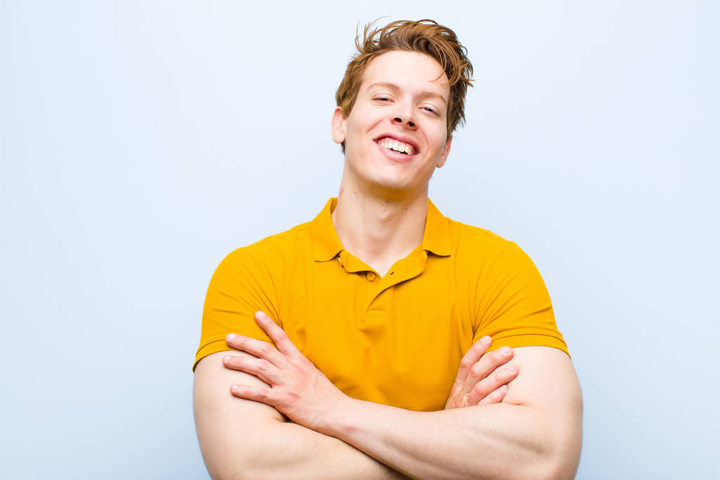 fiatal vörös hajú férfi néz ki, mint egy boldog, büszke és elégedett achiever mosolygó karokkal keresztbe kék fal - Fotó, kép