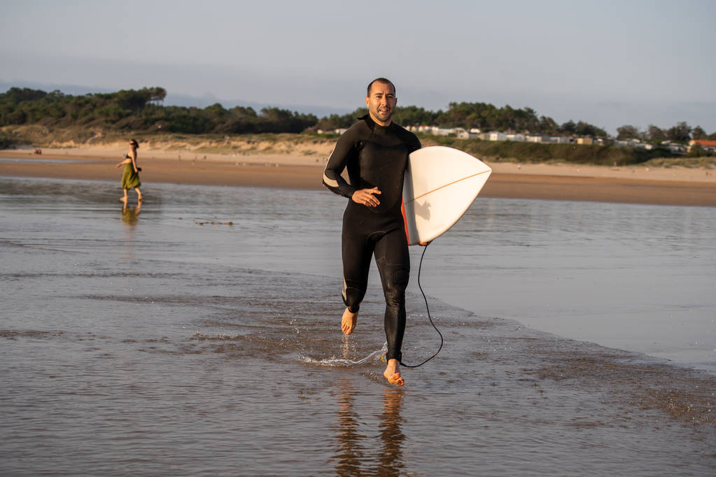 Atrakcyjny surfer z deski surfingowej na plaży surfing o zachodzie słońca lub wschodu słońca. Sport ekstremalny, sporty wodne na świeżym powietrzu, wakacje surf i koncepcja stylu przygody. - Zdjęcie, obraz
