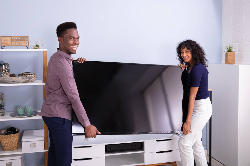 Πλευρική όψη του νεαρού ζευγαριού ανύψωσης τηλεόραση στο σπίτι - Φωτογραφία, εικόνα