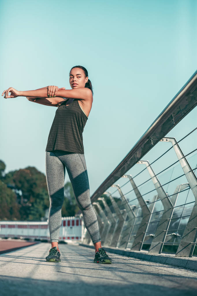 Серьёзная спортсменка на мосту согревает мышцы плеч и рук
 - Фото, изображение