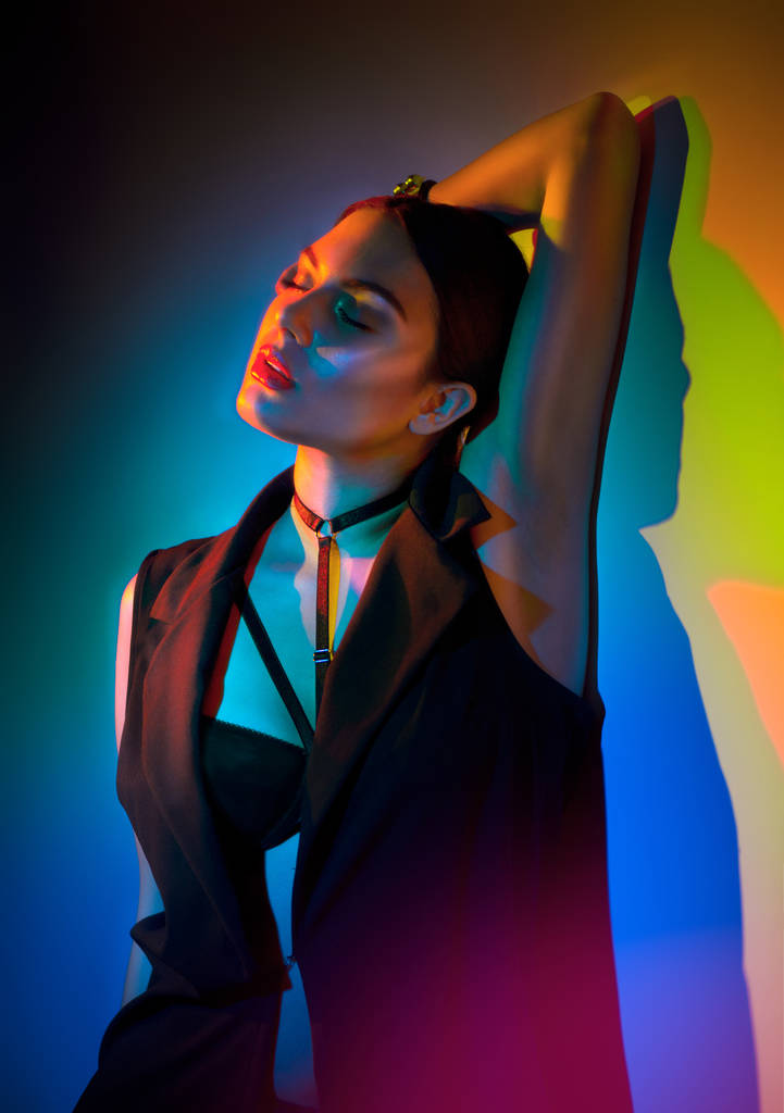 Сексуальная юная брюнетка в черной одежде, модные аксессуары позируют в студии на красочном фоне
 - Фото, изображение