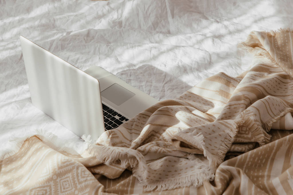 Ordinateur portable sur lit blanc avec un plaid beige. Concept de travail à domicile. Lumière du matin
  - Photo, image