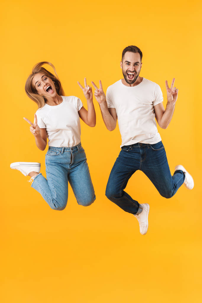 Image of cheerful couple jumping and showing peace sign at camera - Photo, Image