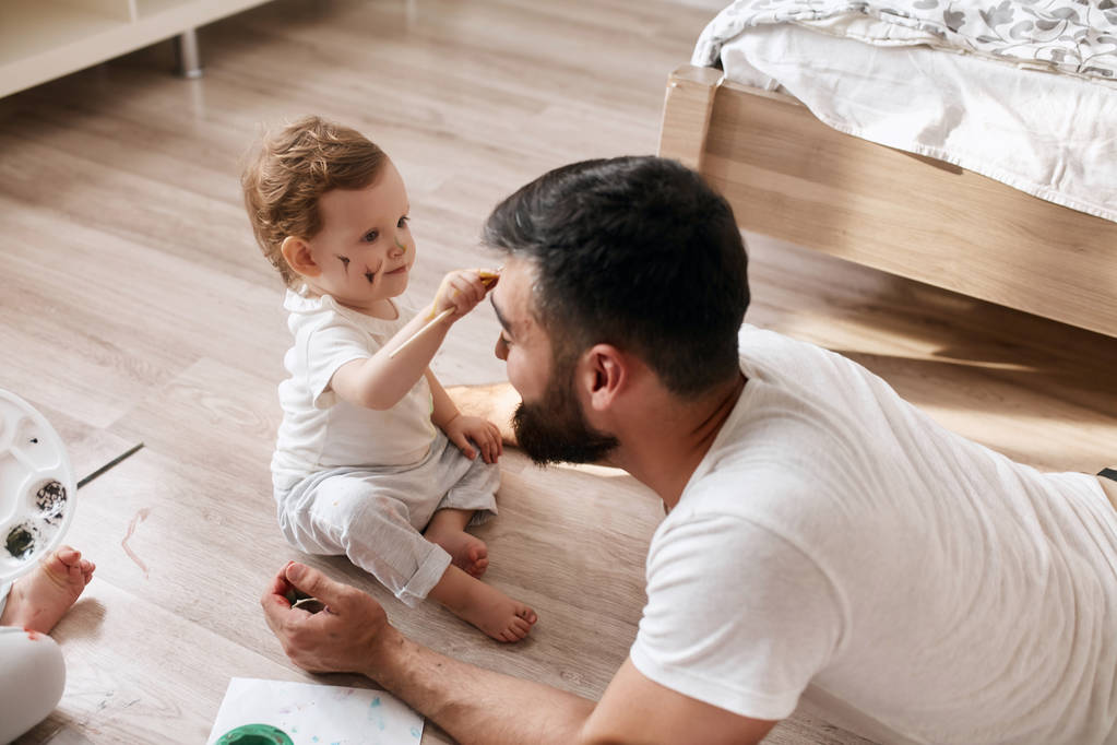 Lustiges kleines Baby bemalt das Gesicht ihres Vaters - Foto, Bild