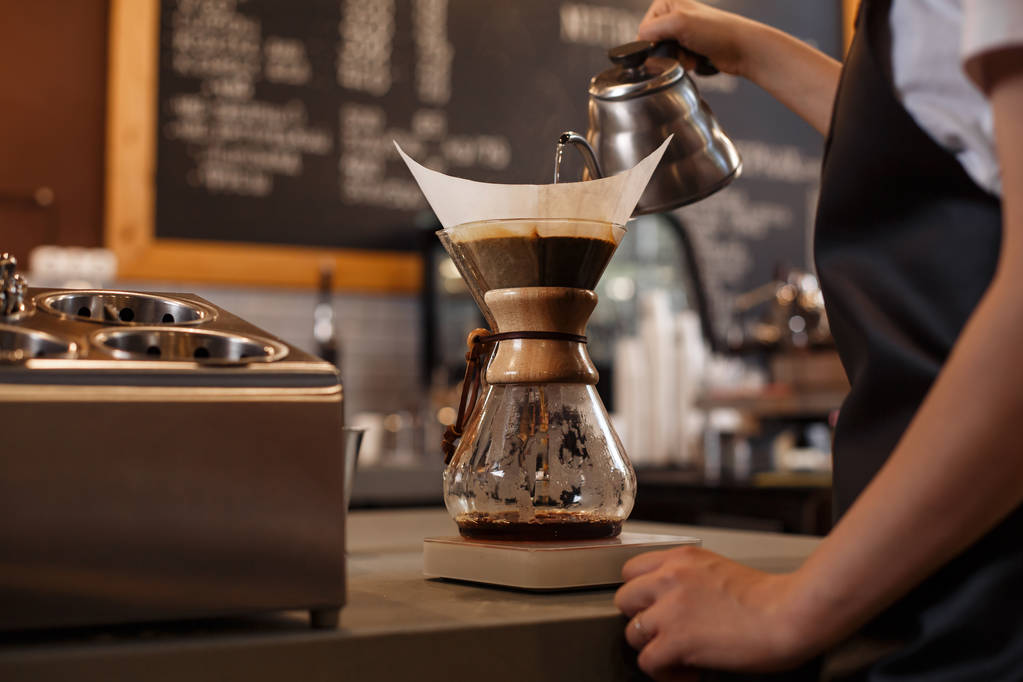 ケメックスを使用してコーヒーを準備プロバリスタは、コーヒーメーカーとドリップケトルを注ぎます。若い女性がコーヒーを作っている。コーヒーを醸造する別の方法。コーヒーショップのコンセプト. - 写真・画像