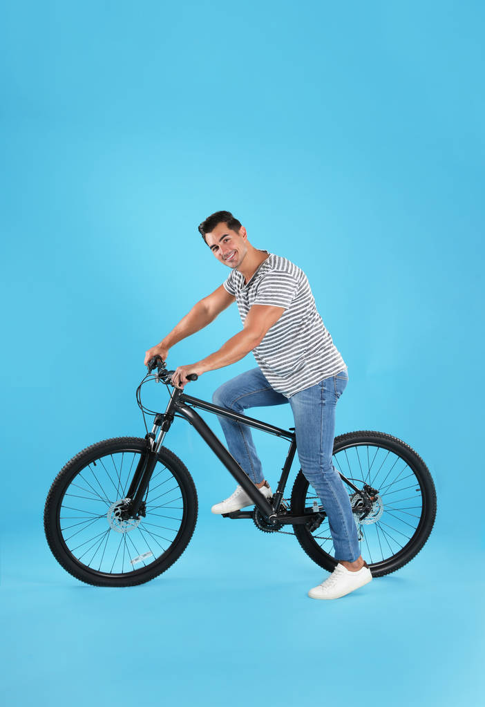 Handsome young man with modern bicycle on light blue background - Photo, Image