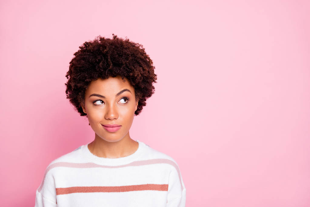 Foto de curiosa chica de piel negra mirando el espacio vacío usando suéter blanco a rayas planeando su vida aislada sobre el fondo de color pastel rosa
 - Foto, imagen