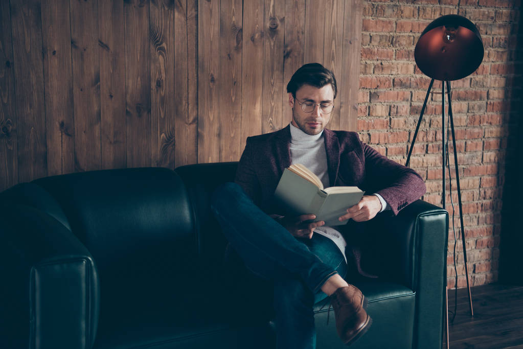 Фото бизнесмена-мачо, держащегося за руки и читающего корпоративную книгу статью о знаменитых вождях, носящих очки стильная водолазка для блейзеров, сидящая на диване современном офисе
 - Фото, изображение