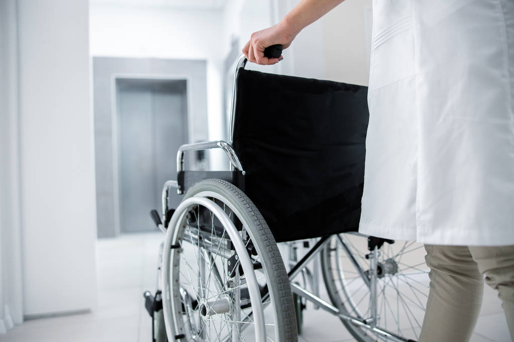 Female doctor with empty wheelchair in lobby - Photo, Image