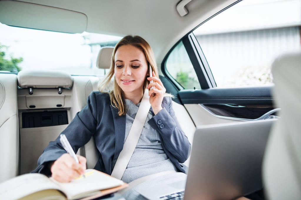Mujer de negocios con teléfono inteligente y portátil sentado en los asientos traseros en coche de taxi
. - Foto, imagen