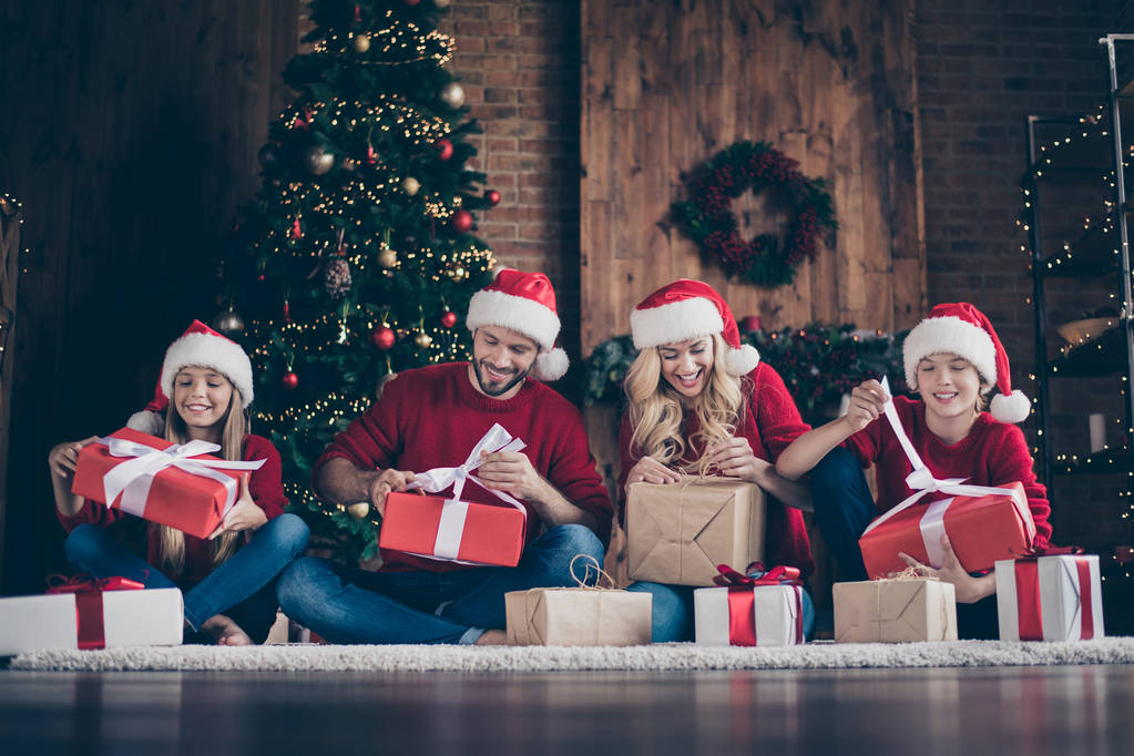 Zdjęcie z Big Family zastanawiał tata Mama siostra brat otwarcie x-mas prezenty siedzi na podłodze w pobliżu ozdobione wieniec światła nowyroku drzewo w pomieszczeniu nosić Santa czapki czerwone swetry - Zdjęcie, obraz