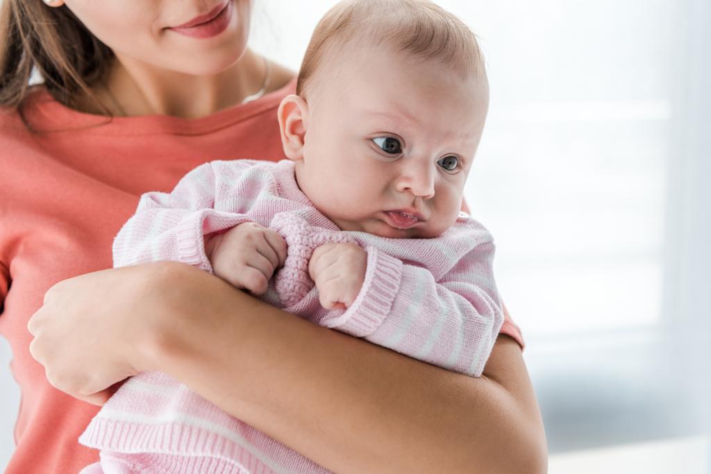 обрізаний вид усміхненої жінки, що тримає в руках чарівну доньку-немовля вдома
  - Фото, зображення
