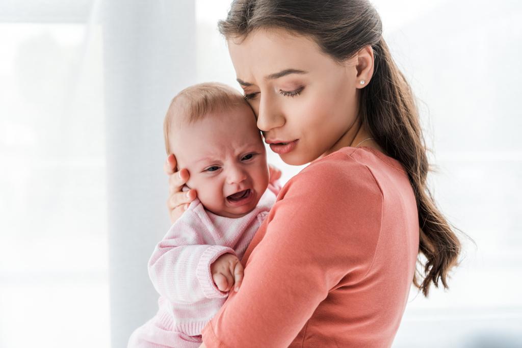 atrakcyjna matka trzymająca w ramionach płaczące niemowlę w domu  - Zdjęcie, obraz