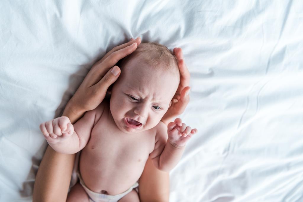 rajattu näkymä äiti koskettaa itkevä vauva tytär makuuhuoneessa
  - Valokuva, kuva