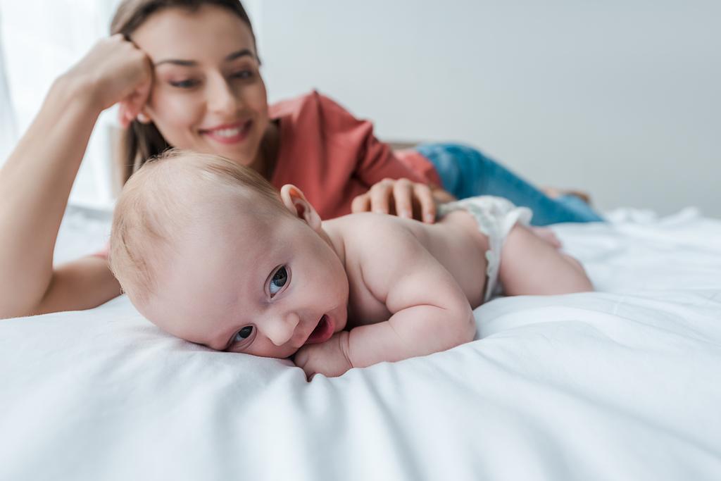 selectieve focus van schattige baby in de buurt vrolijke moeder in de slaapkamer  - Foto, afbeelding