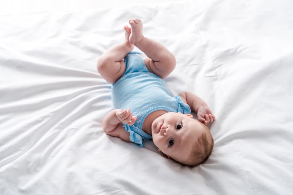 söpö vauva sinisessä vauvan kehonpuvussa makaa sängyssä kotona
  - Valokuva, kuva
