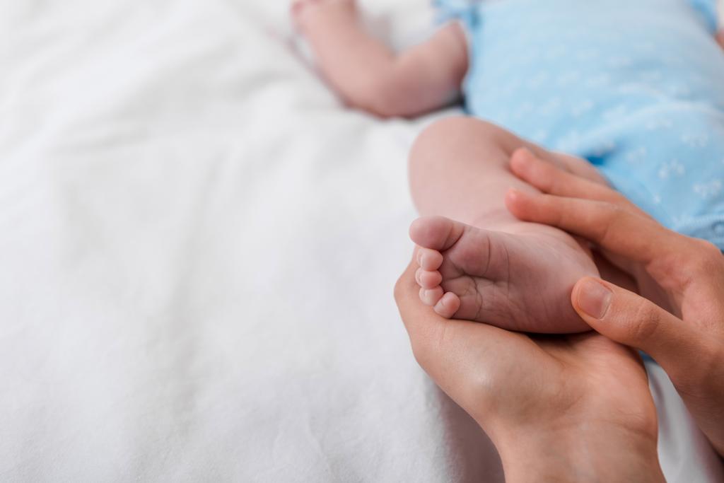rajattu näkymä huolehtiva äiti koskettaa jalka pikkulapsi
  - Valokuva, kuva