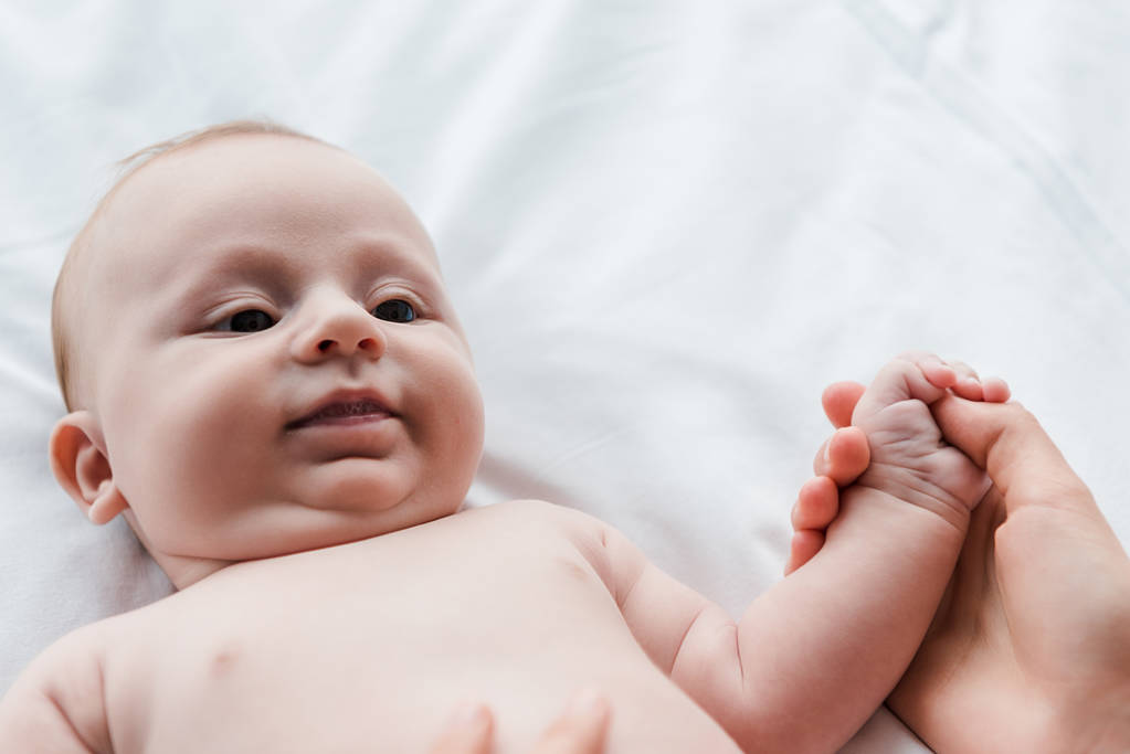 levágott kilátás anya kezében aranyos csecsemő lánya az ágyban  - Fotó, kép