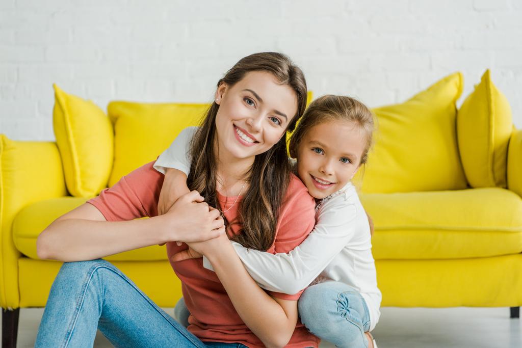 onnellinen lapsi hymyilee halaillessaan iloinen lapsenvahti olohuoneessa
  - Valokuva, kuva