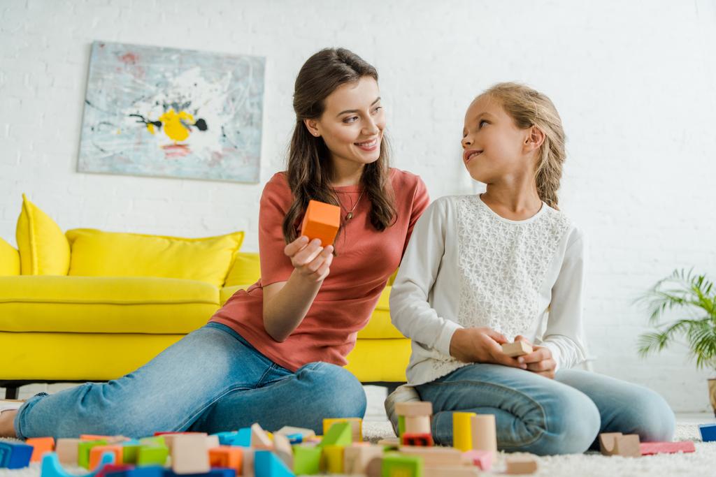 селективное внимание счастливой няни, держащей игрушечный блок рядом с ребенком в гостиной
  - Фото, изображение