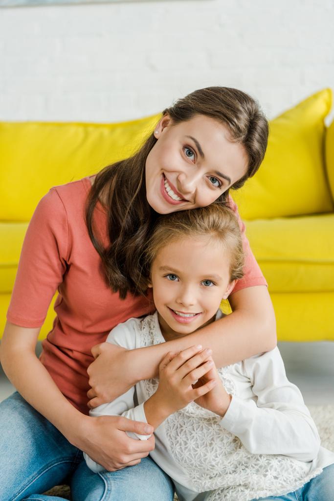 niñera atractiva abrazando niño alegre en la sala de estar
  - Foto, Imagen