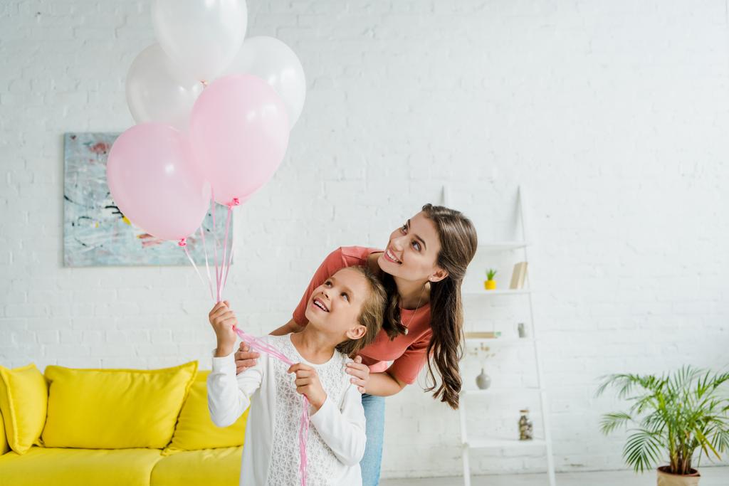 niñera alegre mirando globos rosados cerca de niño feliz
  - Foto, Imagen