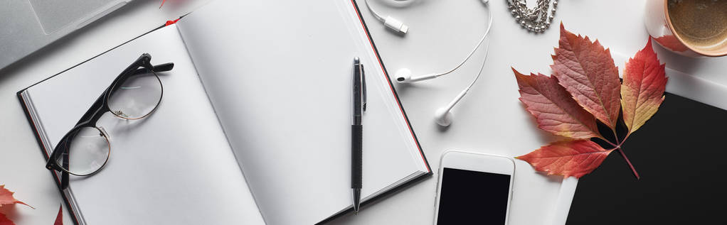panorámás felvétel üres notebook közel toll, szemüveg, okostelefon, digitális tabletta, csésze kávé és vörös levél vadszőlő - Fotó, kép