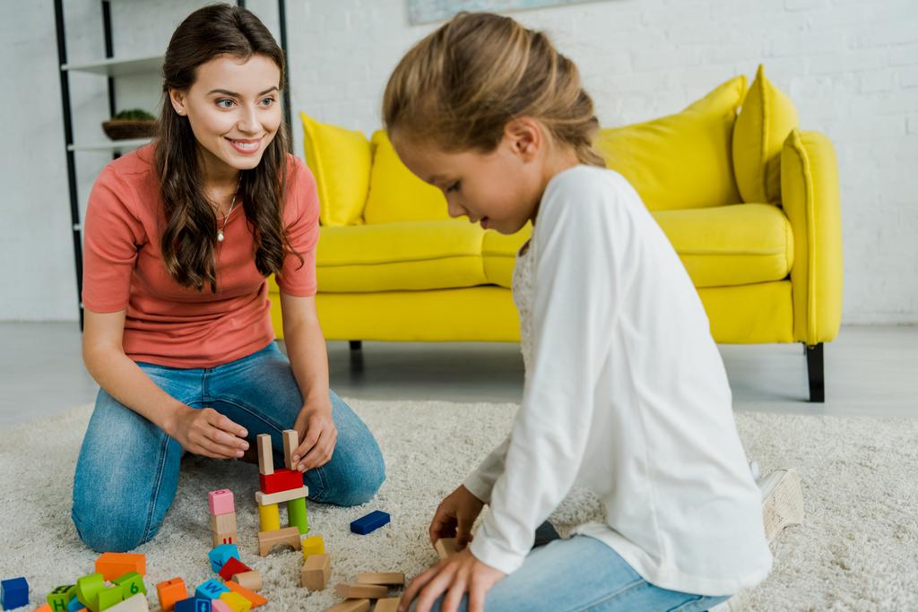 Selektiver Fokus des Babysitters auf Kind in der Nähe von Spielzeugklötzen auf Teppich  - Foto, Bild