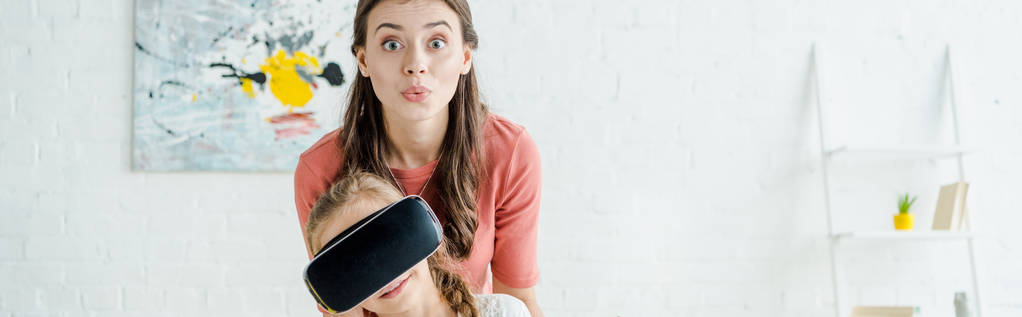 Panoramaaufnahme eines Babysitters, der in Virtual-Reality-Headset auf Kamera in Kindernähe blickt  - Foto, Bild