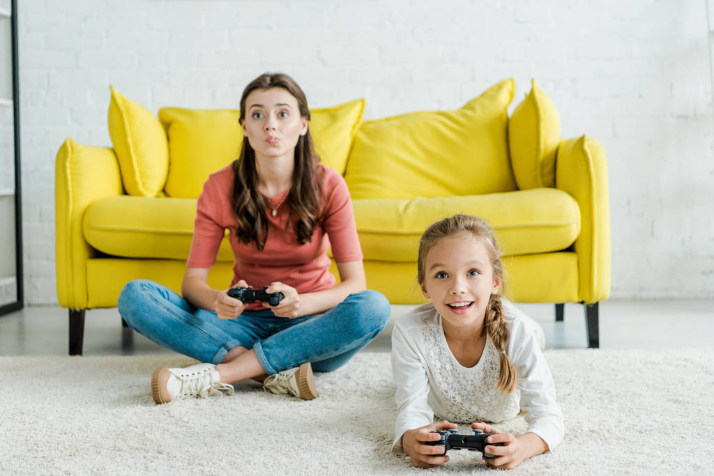 Kiev, Oekraïne - 4 september 2019: babysitter en positief kind spelen videospel in woonkamer  - Foto, afbeelding