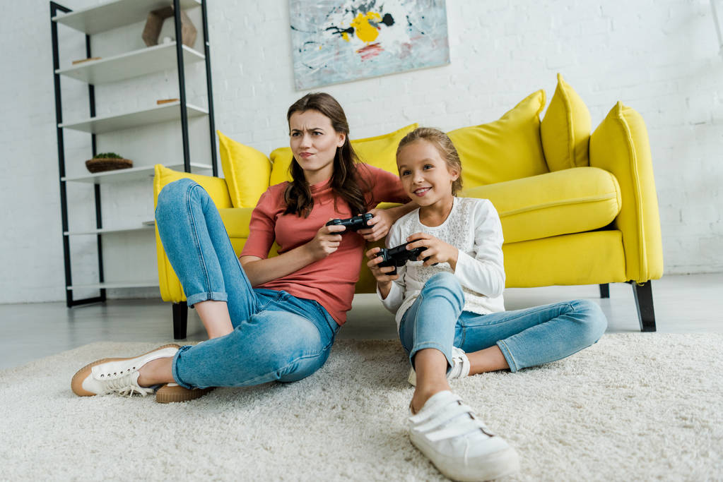 KYIV, UCRAINA - 4 SETTEMBRE 2019: babysitter emotiva e bambino felice seduto sul tappeto e che gioca ai videogiochi in salotto
  - Foto, immagini