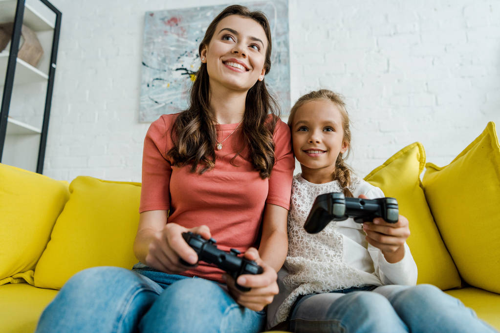 KYIV, UKRAINE - SEPTEMBER 4, 2019: babysitter and happy kid playing video game in living room  - Photo, Image
