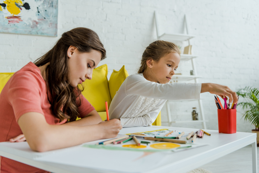 селективный фокус привлекательной няни рисования рядом с симпатичным ребенком в гостиной
  - Фото, изображение