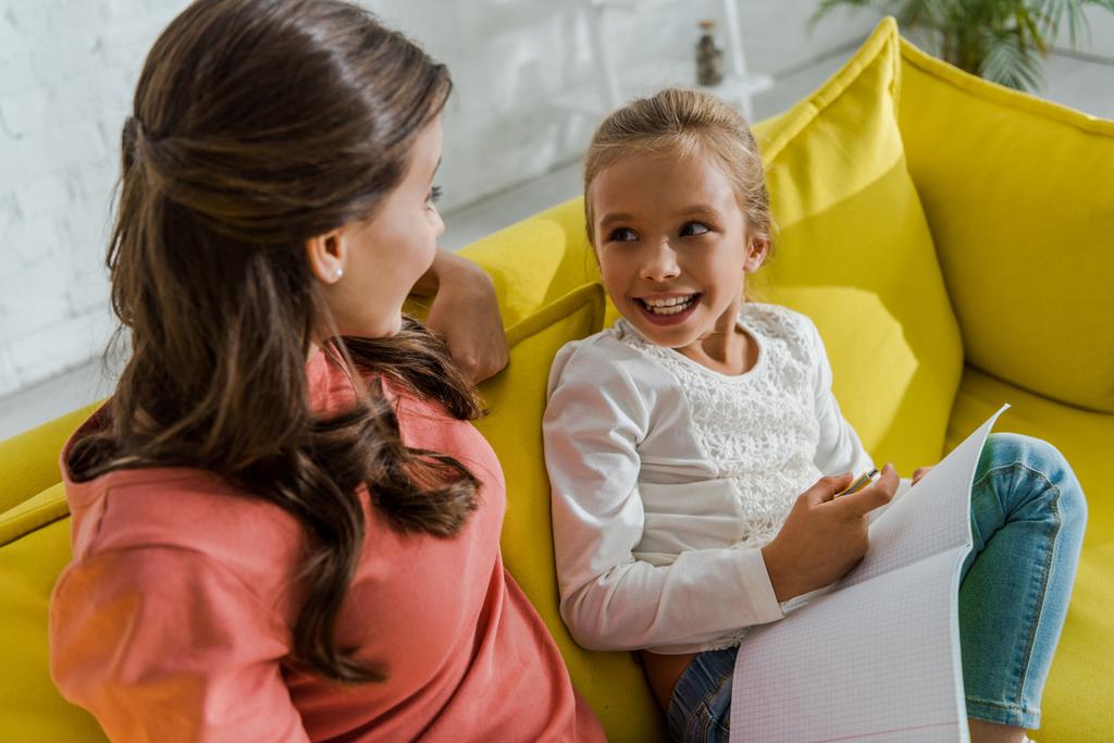 criança feliz segurando notebook e olhando para babá na sala de estar
  - Foto, Imagem
