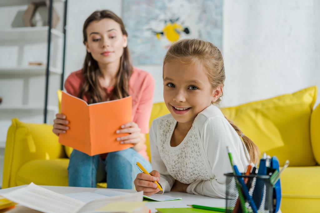 selectieve focus van gelukkig kind studeren in de buurt babysitter lezen boek thuis  - Foto, afbeelding