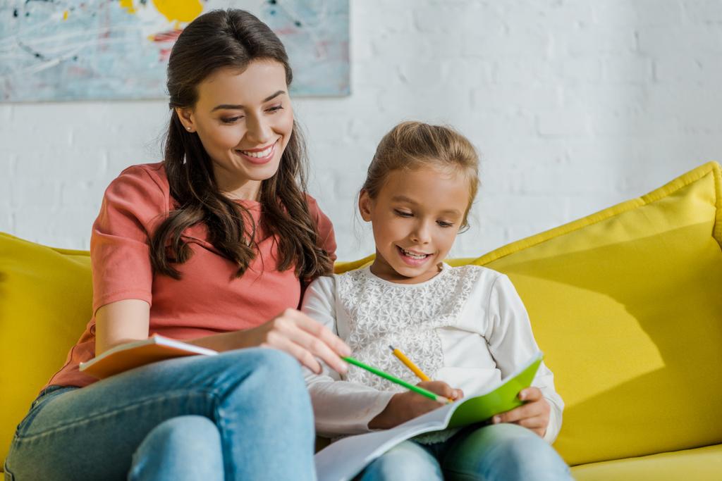 szelektív fókusz boldog bébiszitter ceruzával ül mellett gyerek a nappaliban  - Fotó, kép