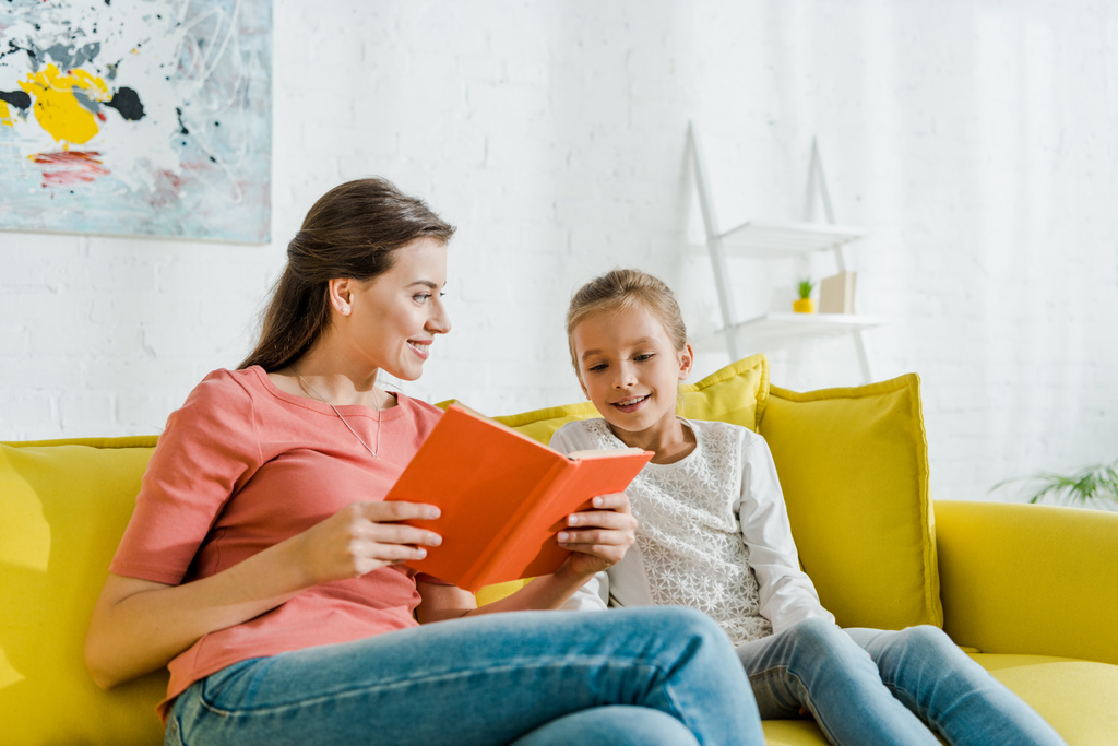 selektywne skupienie szczęśliwego dziecka patrząc na książkę w rękach uśmiechniętej opiekunki  - Zdjęcie, obraz