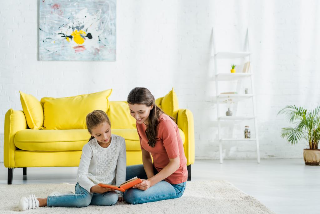 felice bambino lettura libro mentre seduto su tappeto con babysitter
  - Foto, immagini