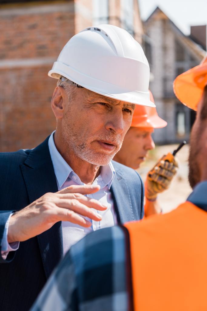 Kypsän liikemiehen valikoiva keskittyminen kypärän eleeseen tarkastellessaan rakentajaa
  - Valokuva, kuva