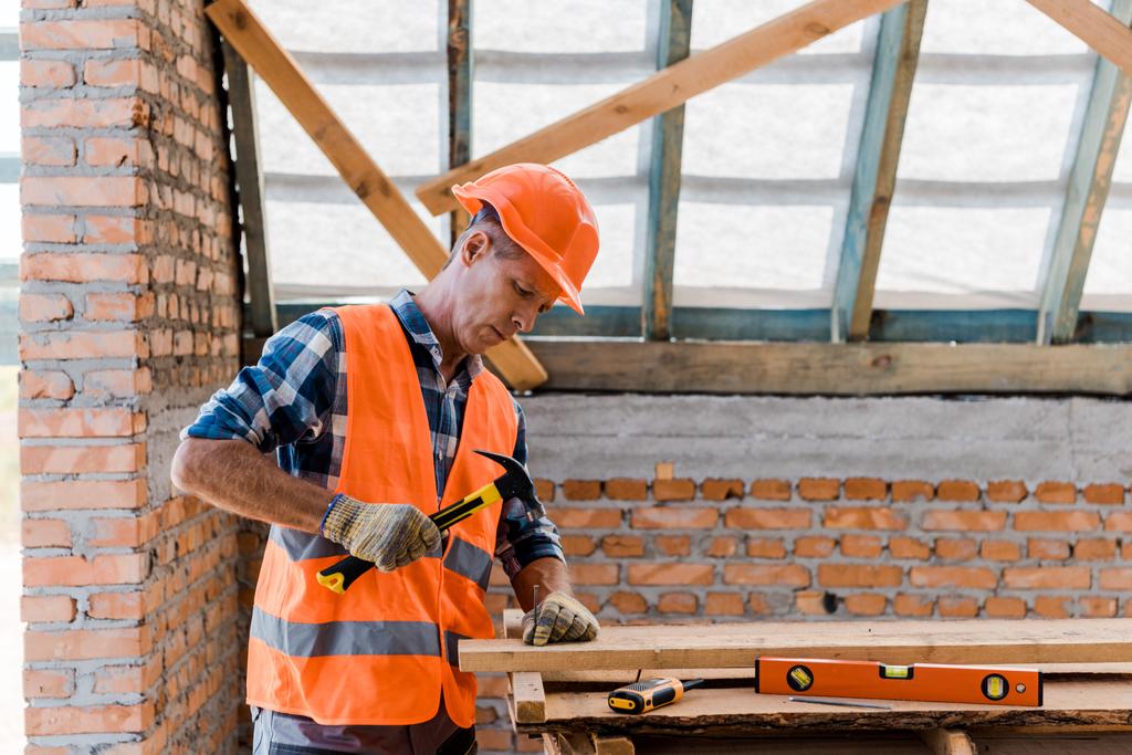 Bauunternehmer mittleren Alters hält Hammer in der Nähe von Nagel - Foto, Bild