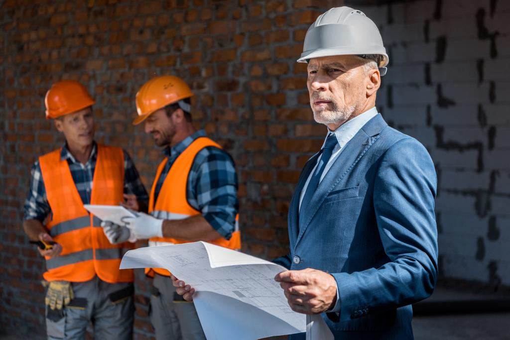 selective focus of businessman holding blueprint near constructors - Photo, Image