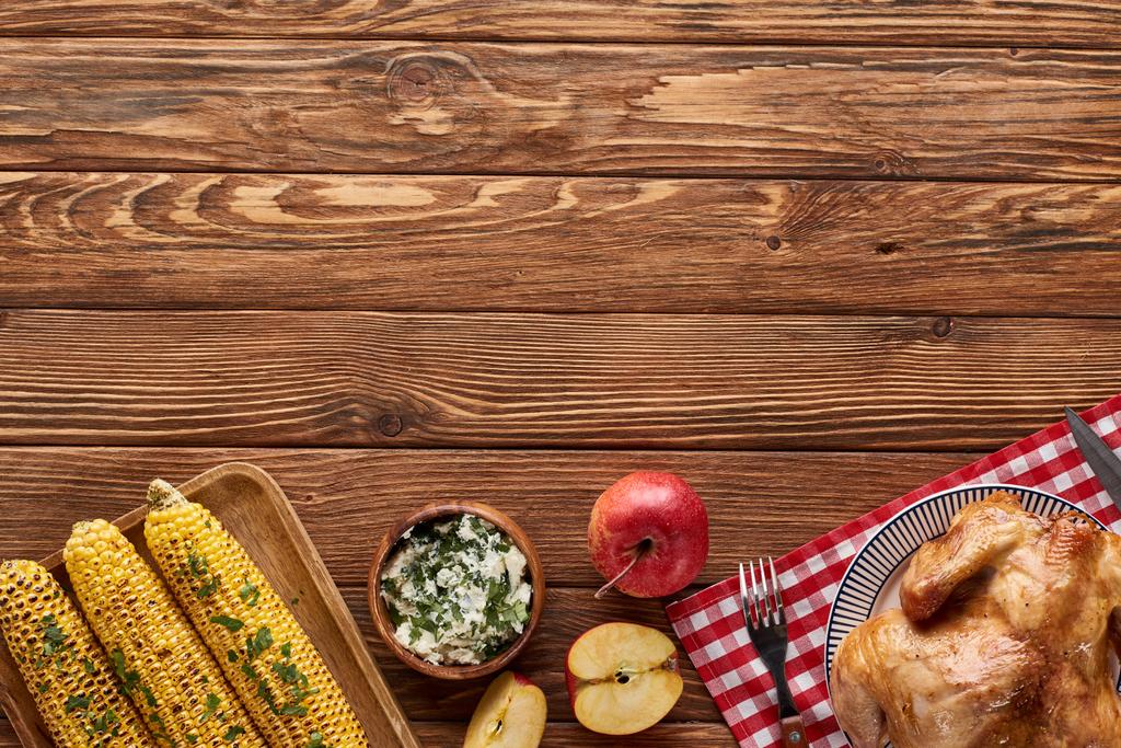 vrchní pohled na pečeného krocana a grilovanou kukuřici podávanou na červeném kostkovaném ubrousku u dřevěného stolu k večeři na Díkůvzdání - Fotografie, Obrázek